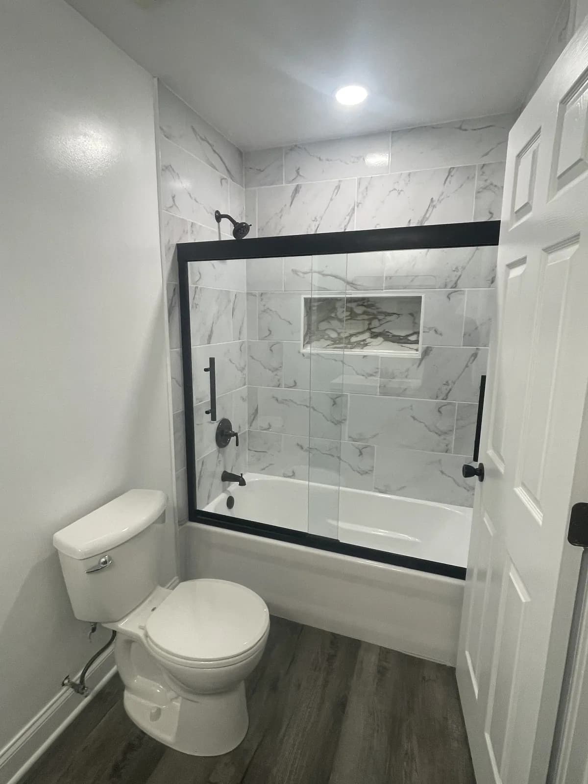 New marble-tiled Aurora tub and shower with black-framed glass after remodeling